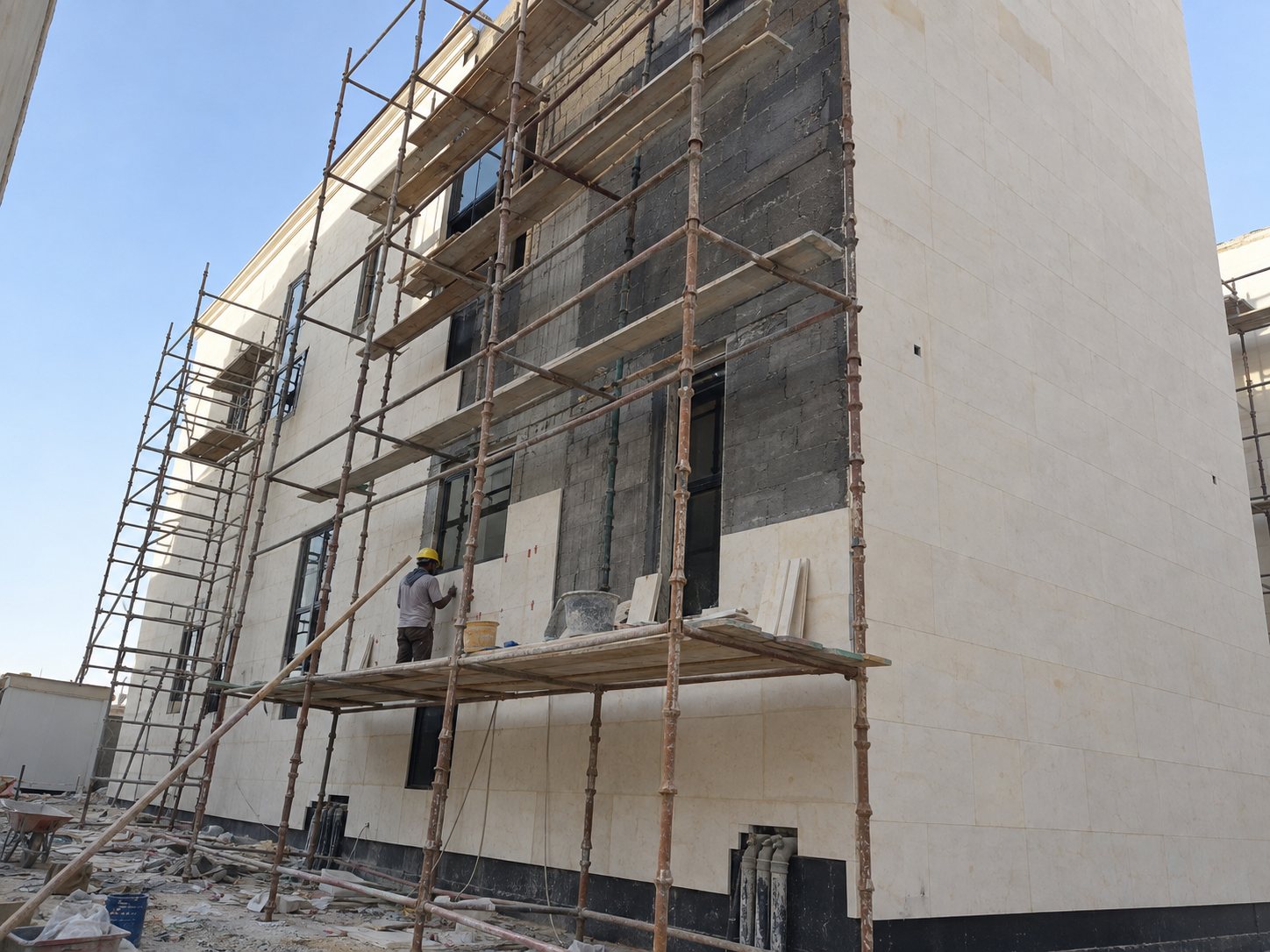 Worker on scaffolding fixing stone cladding to the blockwork façade of a villa under construction