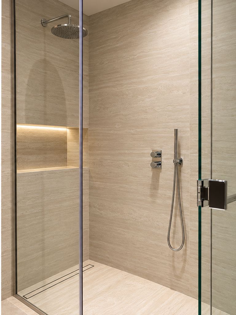 Walk-in shower with stone-clad walls, glass screen, rain shower head and hand shower
